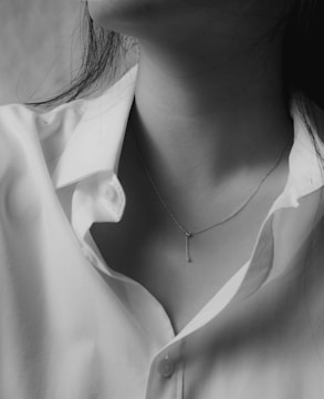 Black and white editorial image of a model wearing a sleek, minimalist necklace under soft lighting.