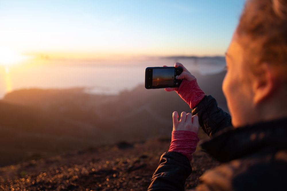 person holding black smartphone taking photo of brown mountain during daytime
