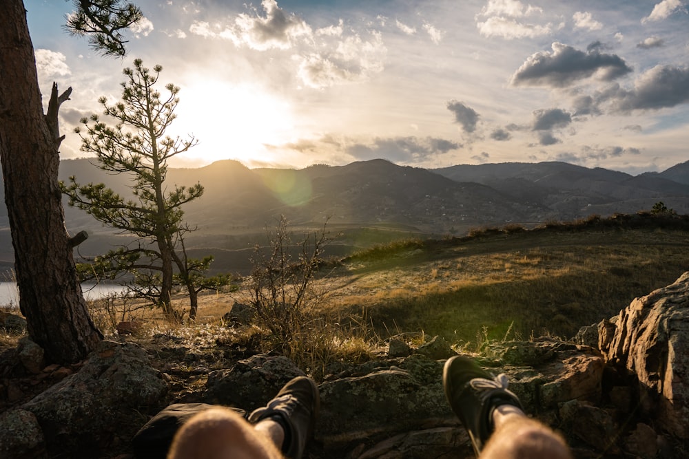 person in gray pants and brown hiking shoes sitting on brown grass field during daytime