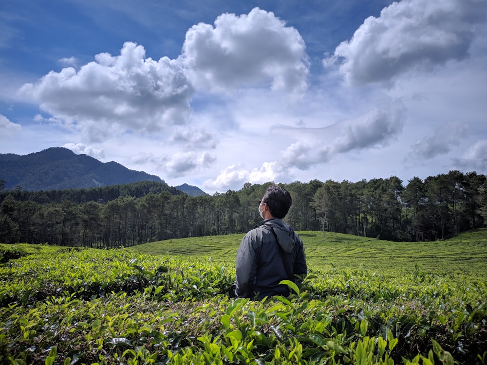 man in black jacket standing on green grass field under white clouds during daytime