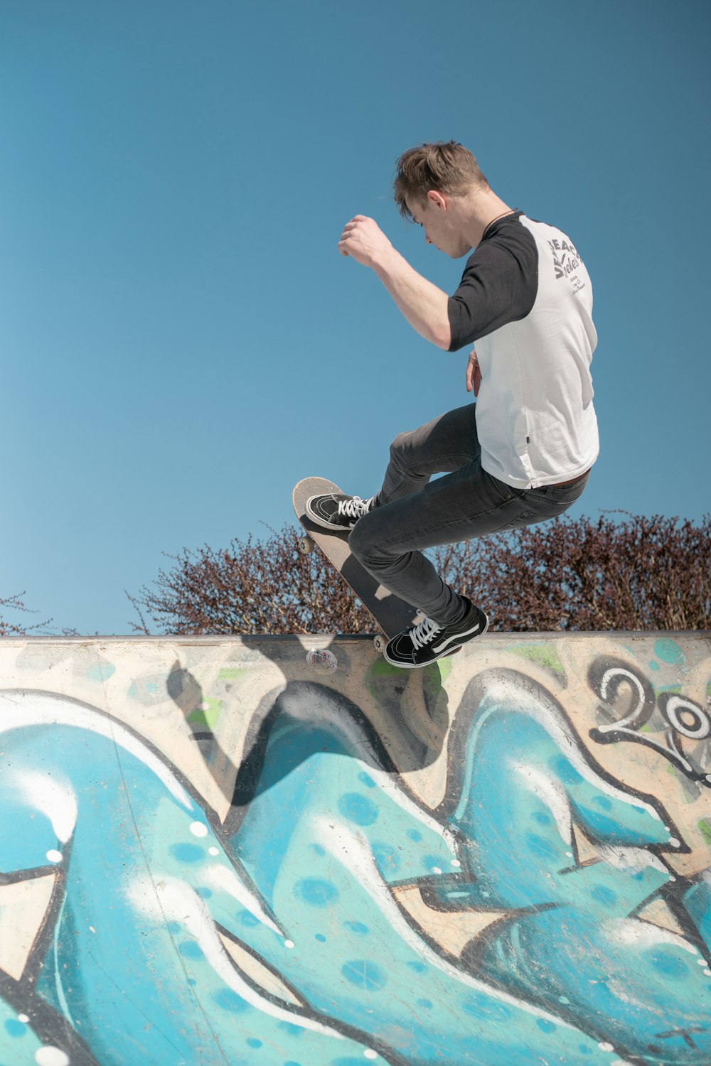 man in white long sleeve shirt and black pants jumping on wall with graffiti during daytime