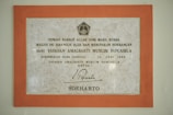 A framed plaque with a beige marble pattern background and a bold orange border featuring Indonesian text. The plaque is a commemoration from Yayasan Amalbakti Muslim Pancasila, dated June 14, 1996, and includes a signature at the bottom.