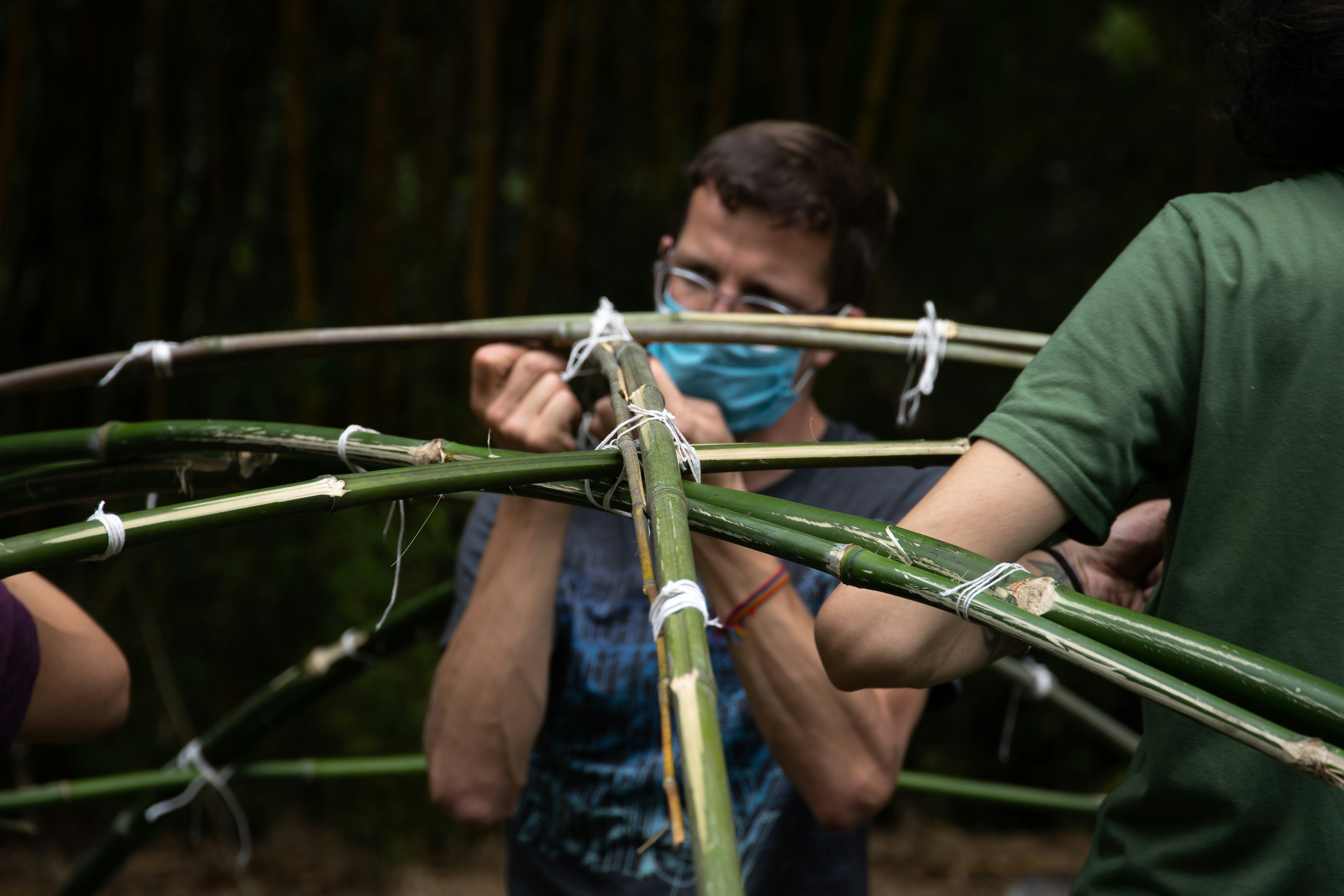 man in green t-shirt holding a green metal bar, People building temazcal tent