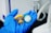 A gloved hand holds two medical filter devices, one yellow and one green. The background features lab equipment and a neutral setting.