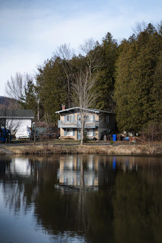 A friendly real estate agent handing keys to a happy family in front of their new home by a peaceful lake.