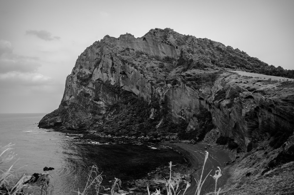 grayscale photo of rocky mountain near body of water