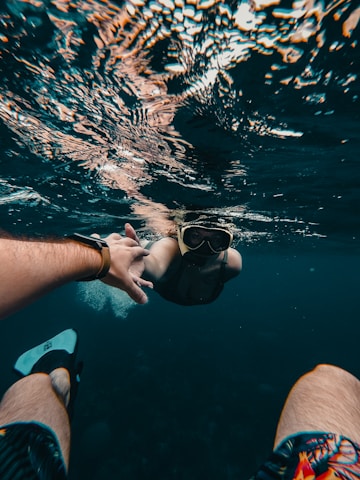 person in blue shorts holding black goggles in water
