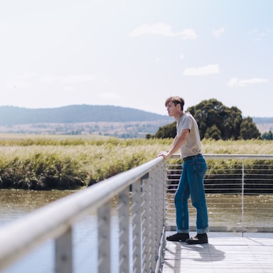 photography poses for men,how to photograph man leaning on railing ; woman in white tank top and blue denim jeans standing on dock during daytime