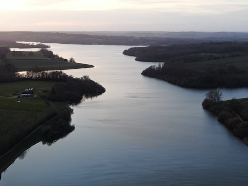 A serene river winding through tall trees and rolling hills under a soft sunset.