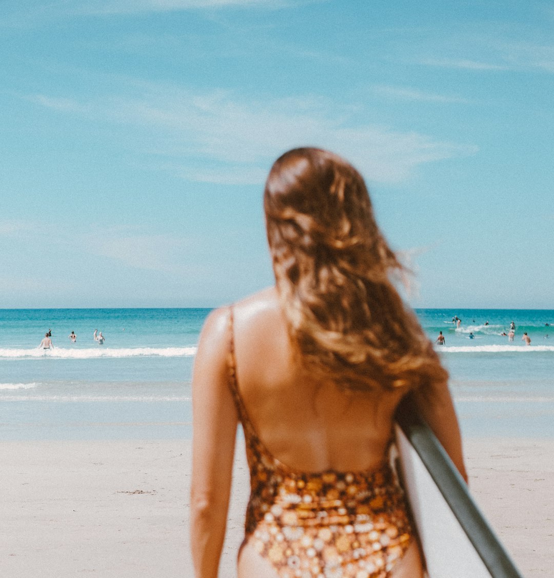 woman in red and white floral spaghetti strap top standing on beach during daytime