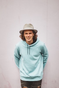 man in teal hoodie standing near white wall