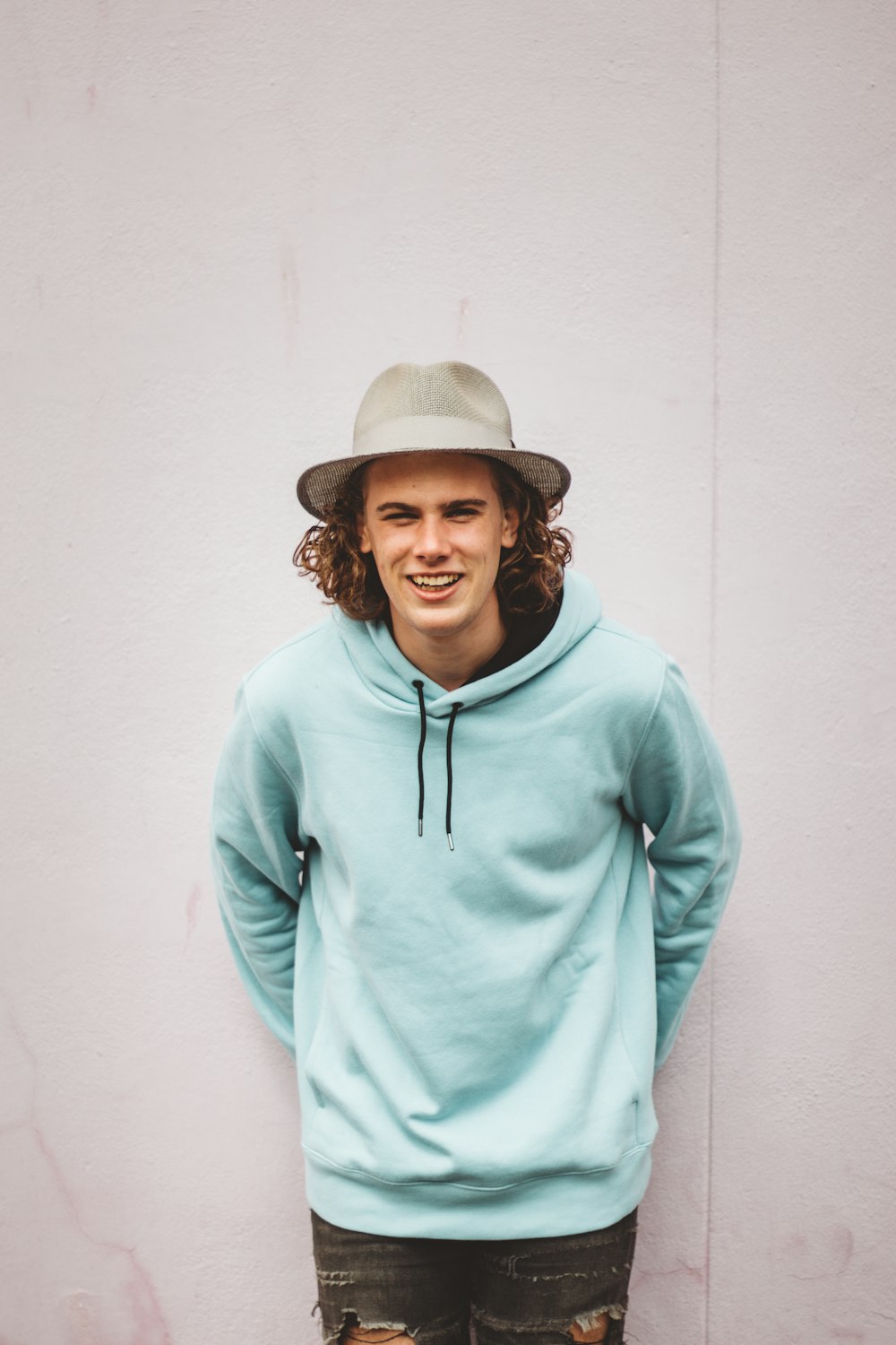 man in teal hoodie standing near white wall