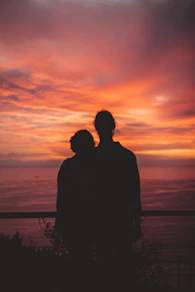 silhouette of man standing near body of water during sunset