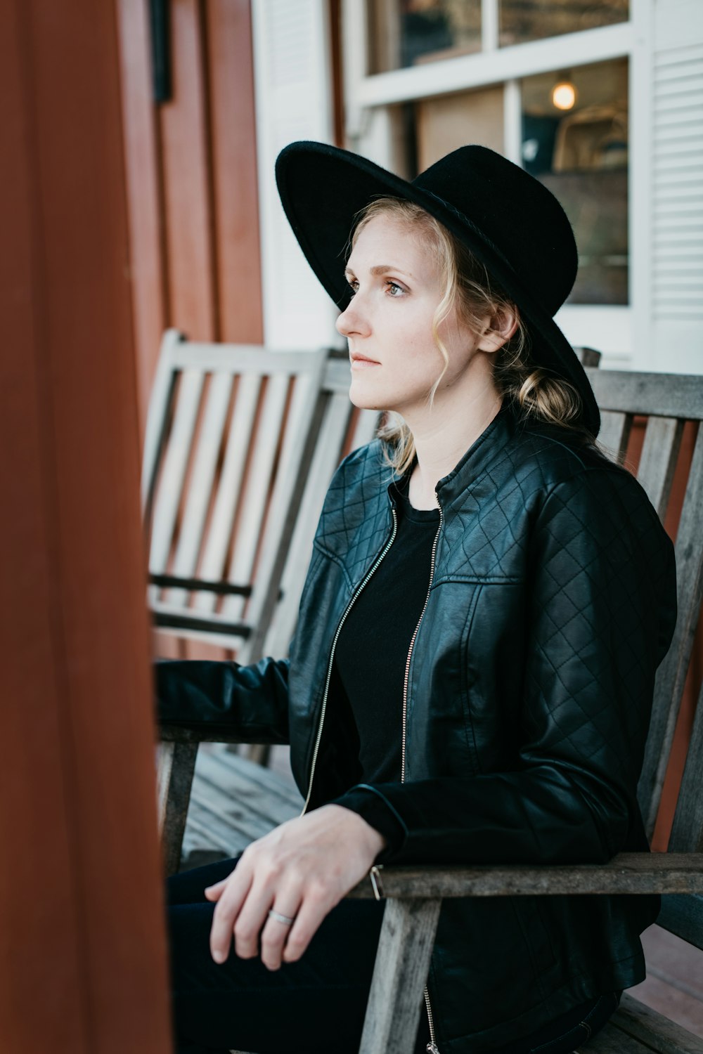 woman in black leather jacket and black hat sitting on brown wooden chair
