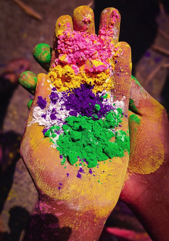 Hands covered in purple, yellow and green Holi powder. Photo by Souvik Laha on Unsplash.