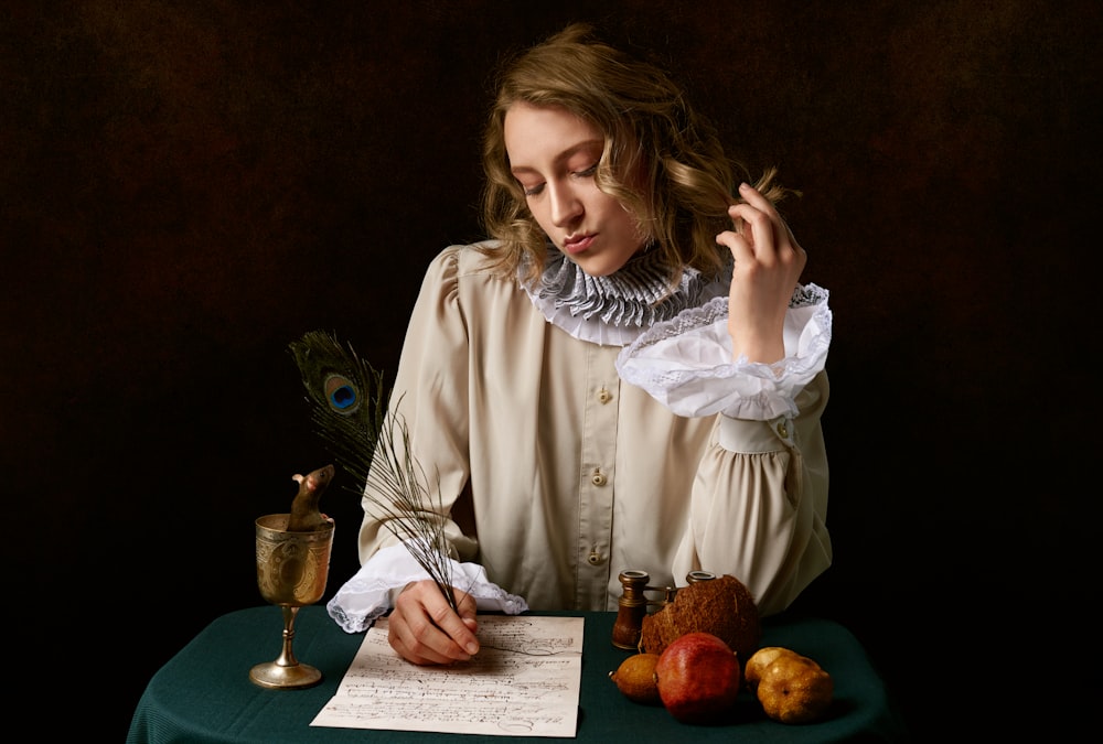 girl in white long sleeve shirt sitting beside table with red apple fruit and clear wine