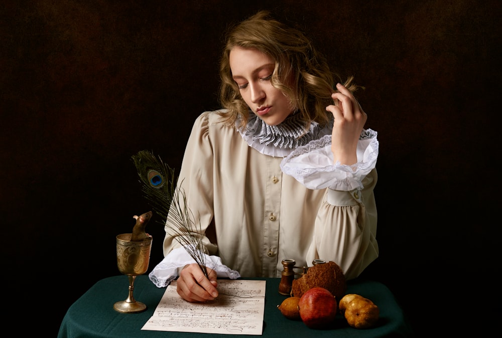 빨간 사과 과일과 맑은 와인이 있는 테이블 옆에 앉아 있는 흰색 긴 소매 셔츠를 입은 소녀