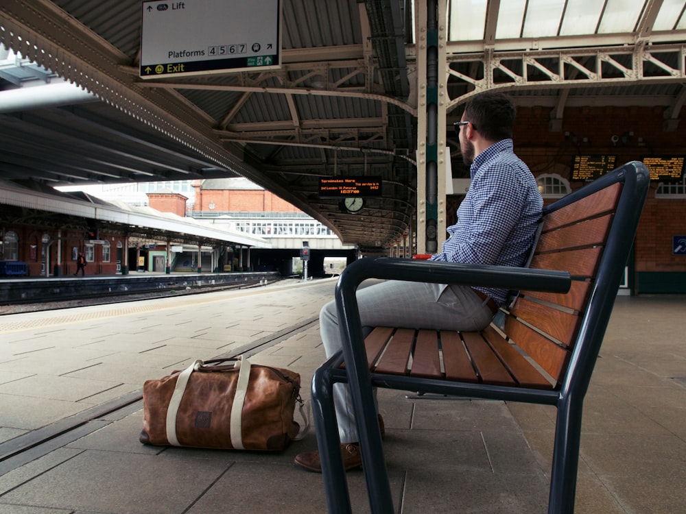 man in blue and white checkered dress shirt sitting on brown wooden bench