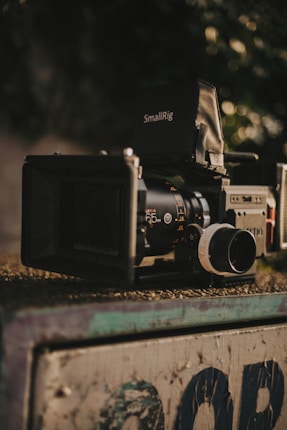 A professional camera setup is positioned on a surface, equipped with various attachments including a lens, a follow focus system, and a matte box. The brand 'SmallRig' is visible on one of the components. The background is softly blurred, focusing attention on the camera.