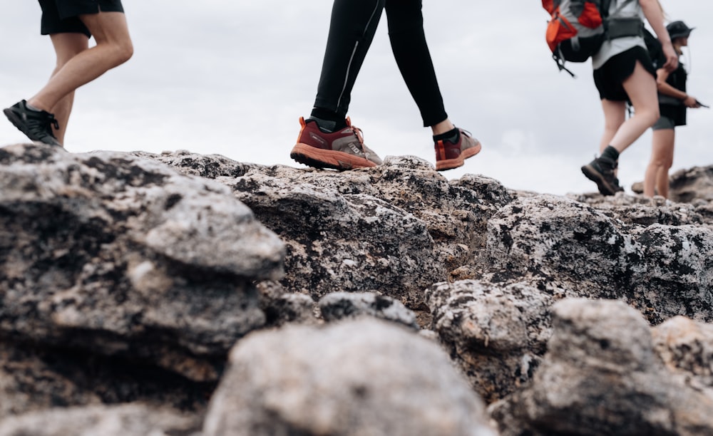 person in black pants and orange and black nike sneakers standing on rocky ground during daytime