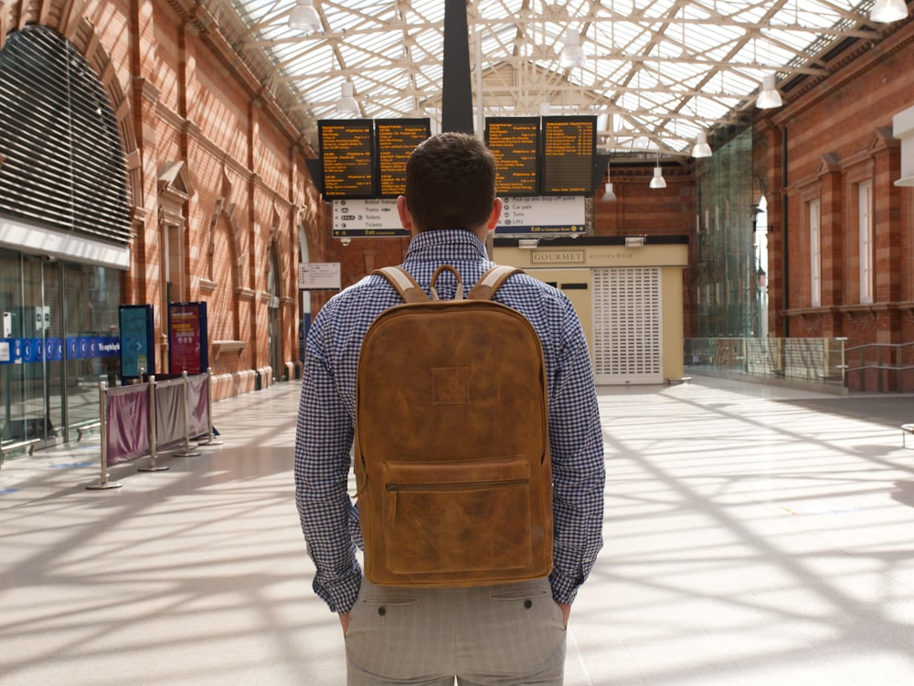 man in brown and black backpack standing on sidewalk during daytime