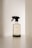 A transparent spray bottle with a black trigger nozzle rests on a solid surface. The bottle is labeled with the brand name 'kinfill' and contains a clear liquid. The background is minimalist with soft lighting that casts gentle shadows on the surface.