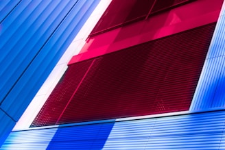 A modern architectural facade featuring bold color contrasts with vertical and horizontal lines. The design incorporates sections of vibrant red, blue, and white panels, creating a striking and dynamic composition.