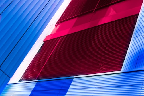 A modern architectural facade featuring bold color contrasts with vertical and horizontal lines. The design incorporates sections of vibrant red, blue, and white panels, creating a striking and dynamic composition.