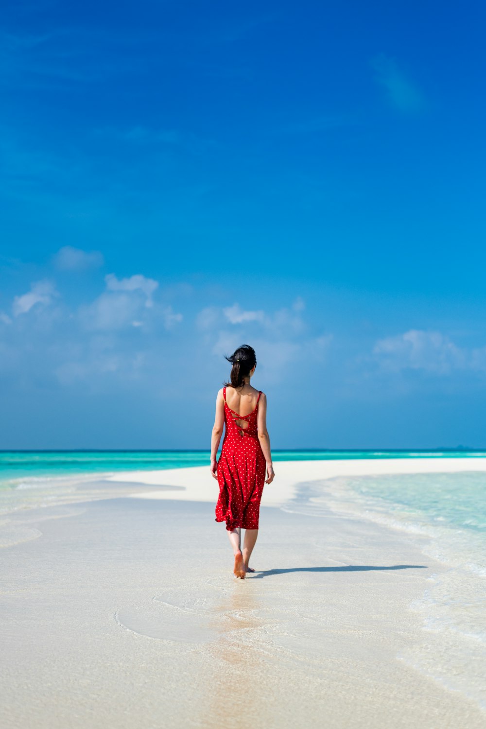 donna in vestito rosso in piedi sulla spiaggia durante il giorno