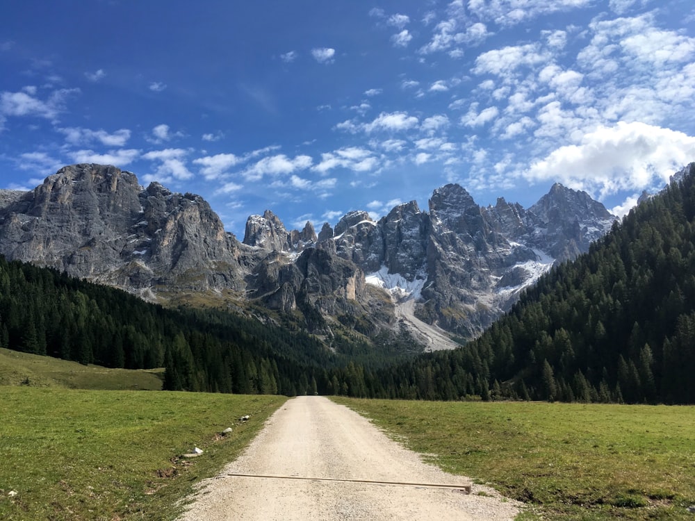 gray concrete road between green grass field near mountain under blue and white cloudy sky during