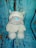 A plush toy of a dog with a white body, gray snout, and blue nose is placed against a backdrop resembling cracked, painted blue and brown wood.