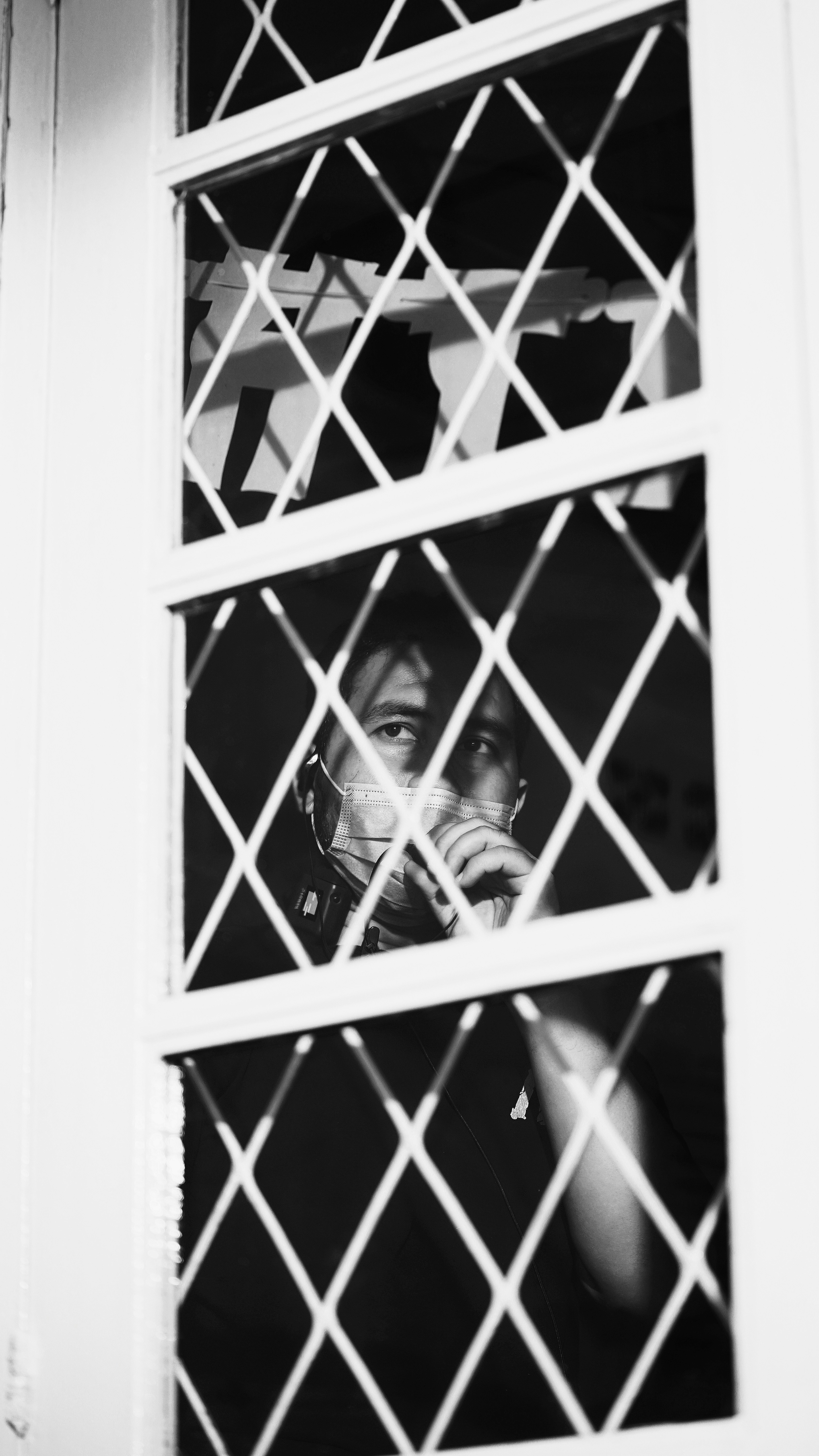 grayscale photo of woman in stripe shirt standing behind metal fence