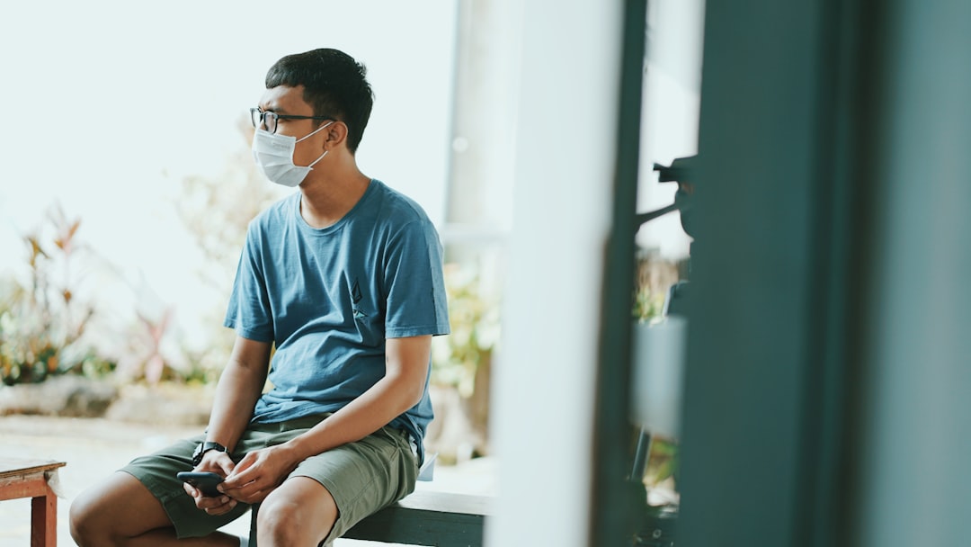 man in blue crew neck t-shirt and gray shorts sitting on white wooden bench during