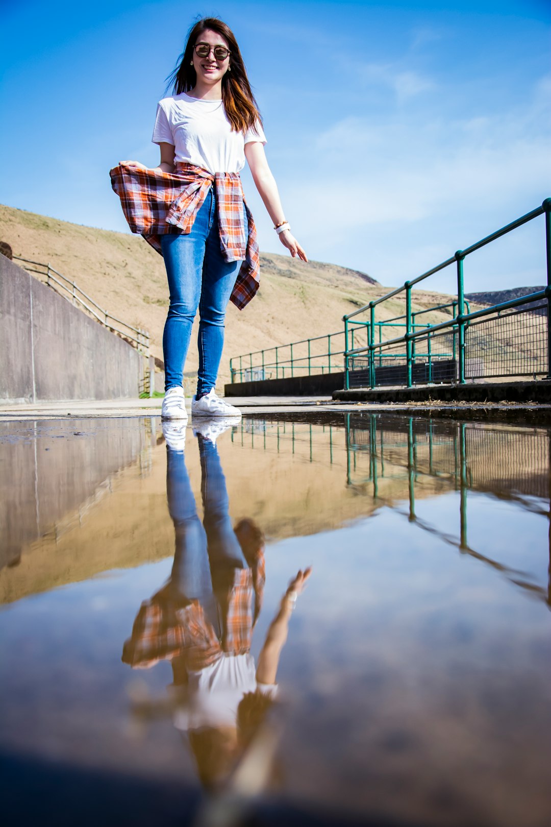 woman in white and brown plaid shirt and blue denim jeans standing on bridge during daytime