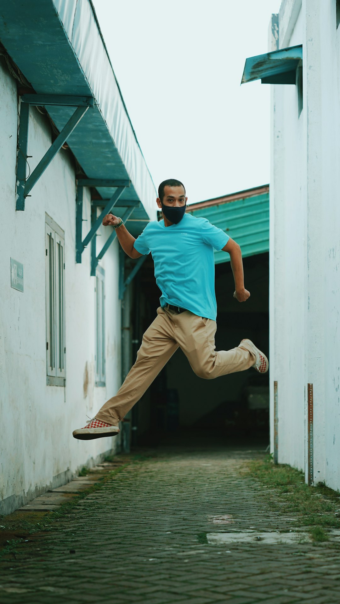 man in blue t-shirt and brown pants jumping on gray wall during daytime