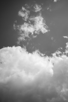 The image features a sky filled with fluffy clouds. The clouds vary in density, with some areas more concentrated and others wispy and thin. The color palette is monochromatic, emphasizing shades of gray.