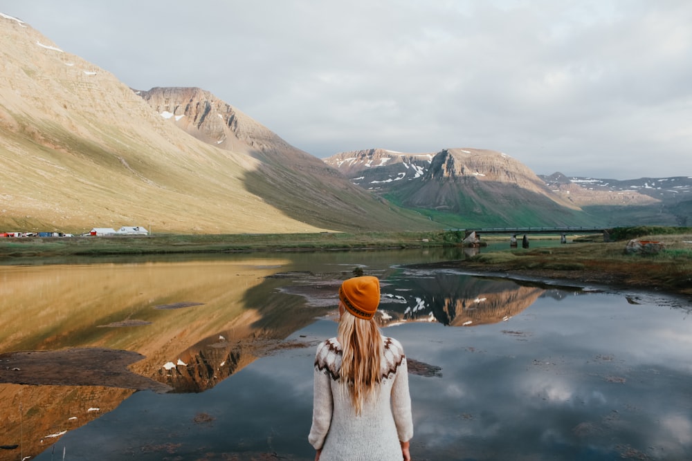 woman in white sweater standing near lake during daytime