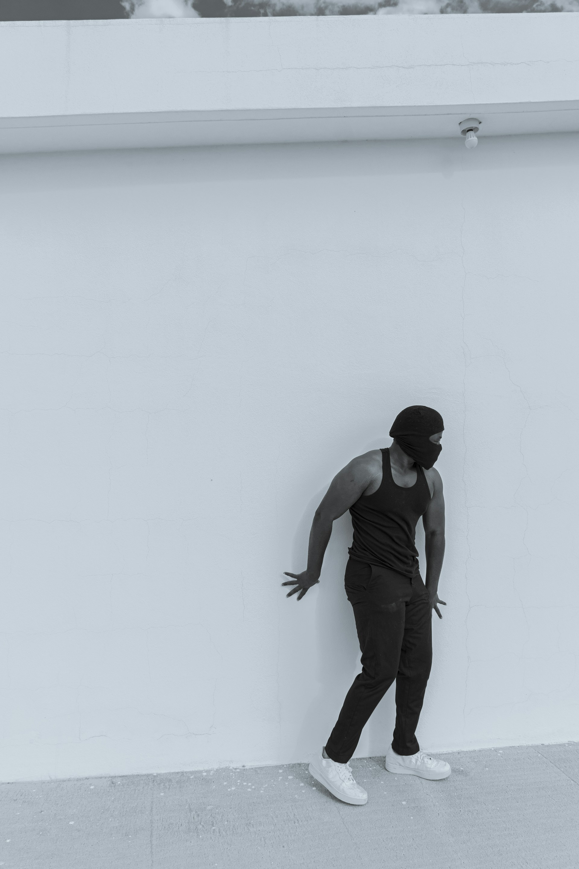 Black and white photo of a person wearing a simple, minimal casual outfit standing against a textured wall.
