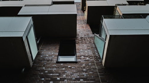 A modern architectural design featuring a series of protruding balcony structures against a brick facade. The perspective is looking upward, showcasing the geometric alignment and sharp lines of the building elements, combined with glass railings that allow ambient light to reflect.