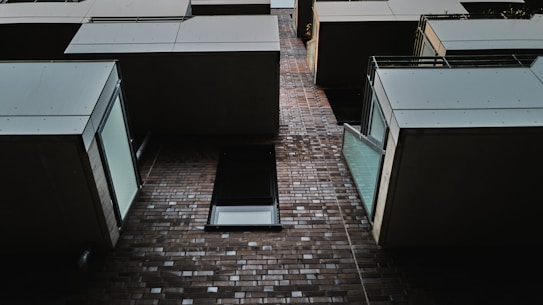 A modern architectural design featuring a series of protruding balcony structures against a brick facade. The perspective is looking upward, showcasing the geometric alignment and sharp lines of the building elements, combined with glass railings that allow ambient light to reflect.