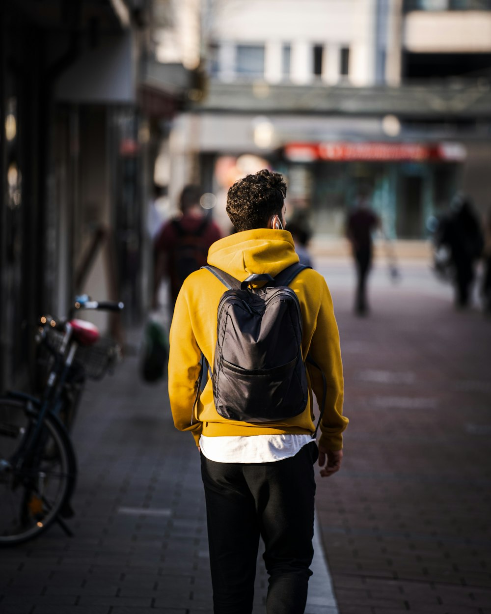 Mann in gelbem und schwarzem Rucksack tagsüber auf dem Bürgersteig