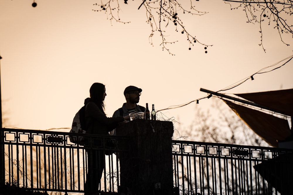 Silhouette von 2 Männern, die während des Sonnenuntergangs am Zaun stehen