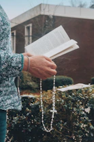 Close-up of hands holding a rosary over an open book with gentle sunlight.
