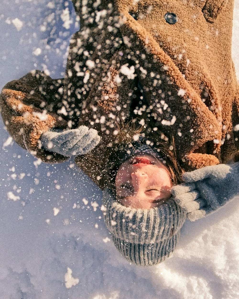 woman in brown coat lying on snow covered ground during daytime