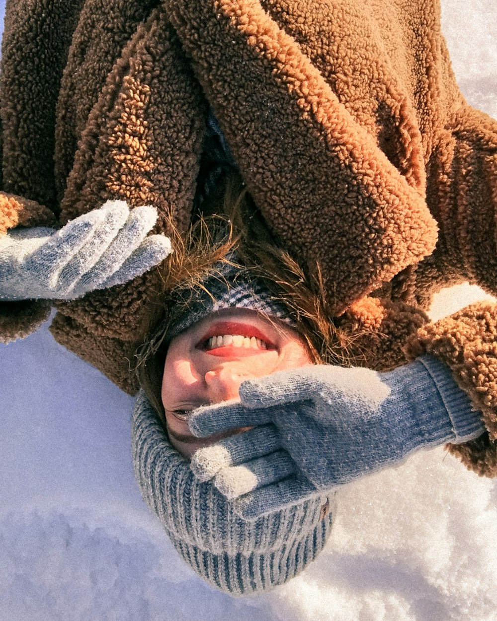 woman in brown and white sweater lying on snow covered ground