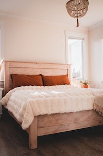 Cozy wooden bed frame with soft white linens and a warm throw blanket.