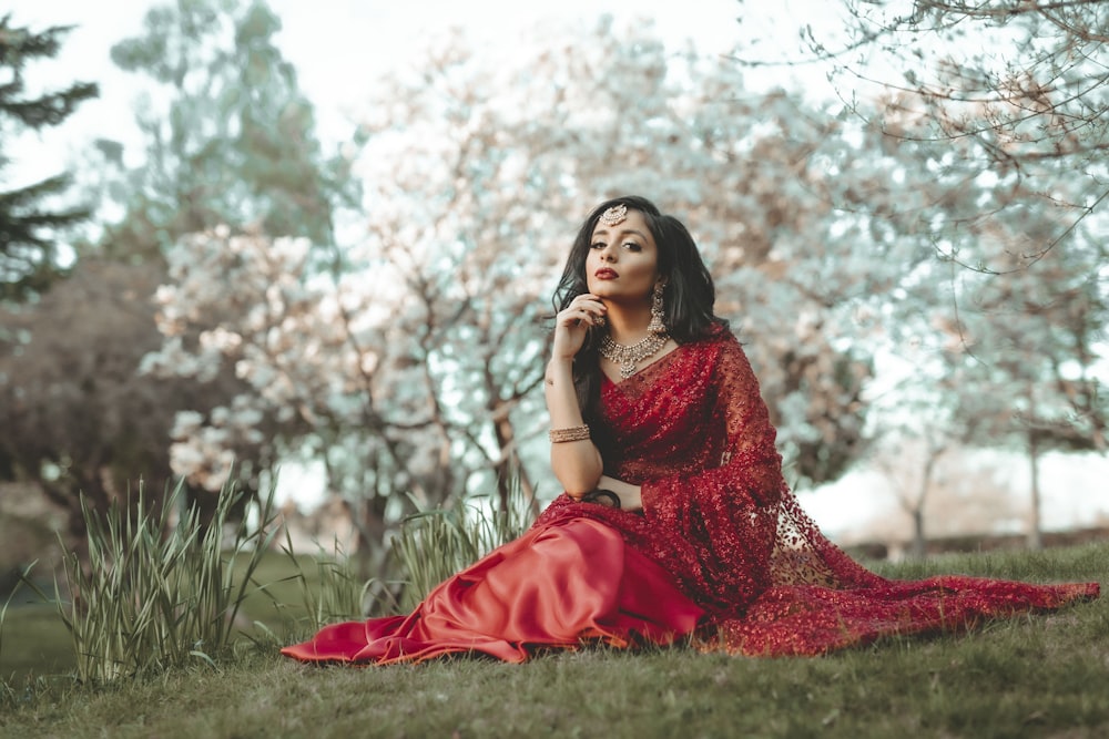 Mujer en vestido rojo sentada en el campo de hierba