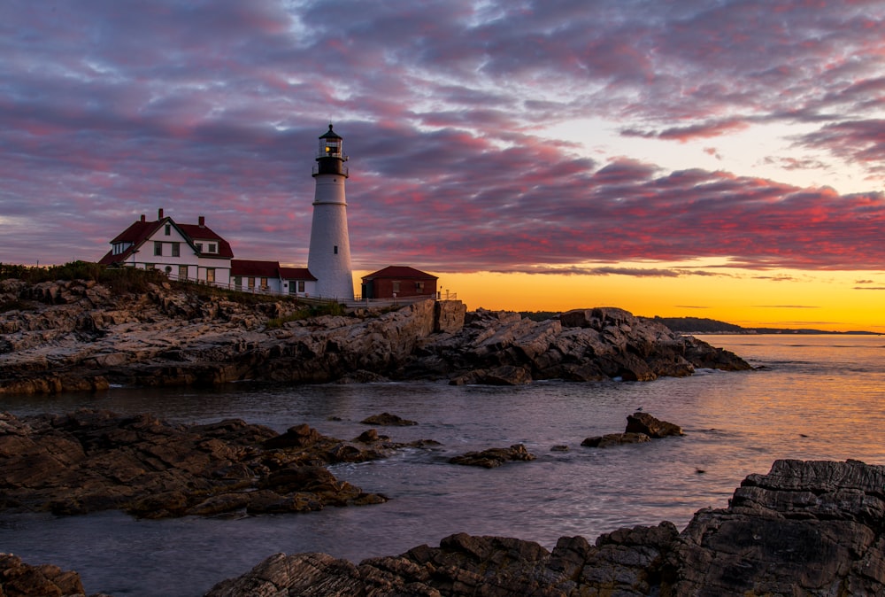 white and black lighthouse on rocky shore during sunset