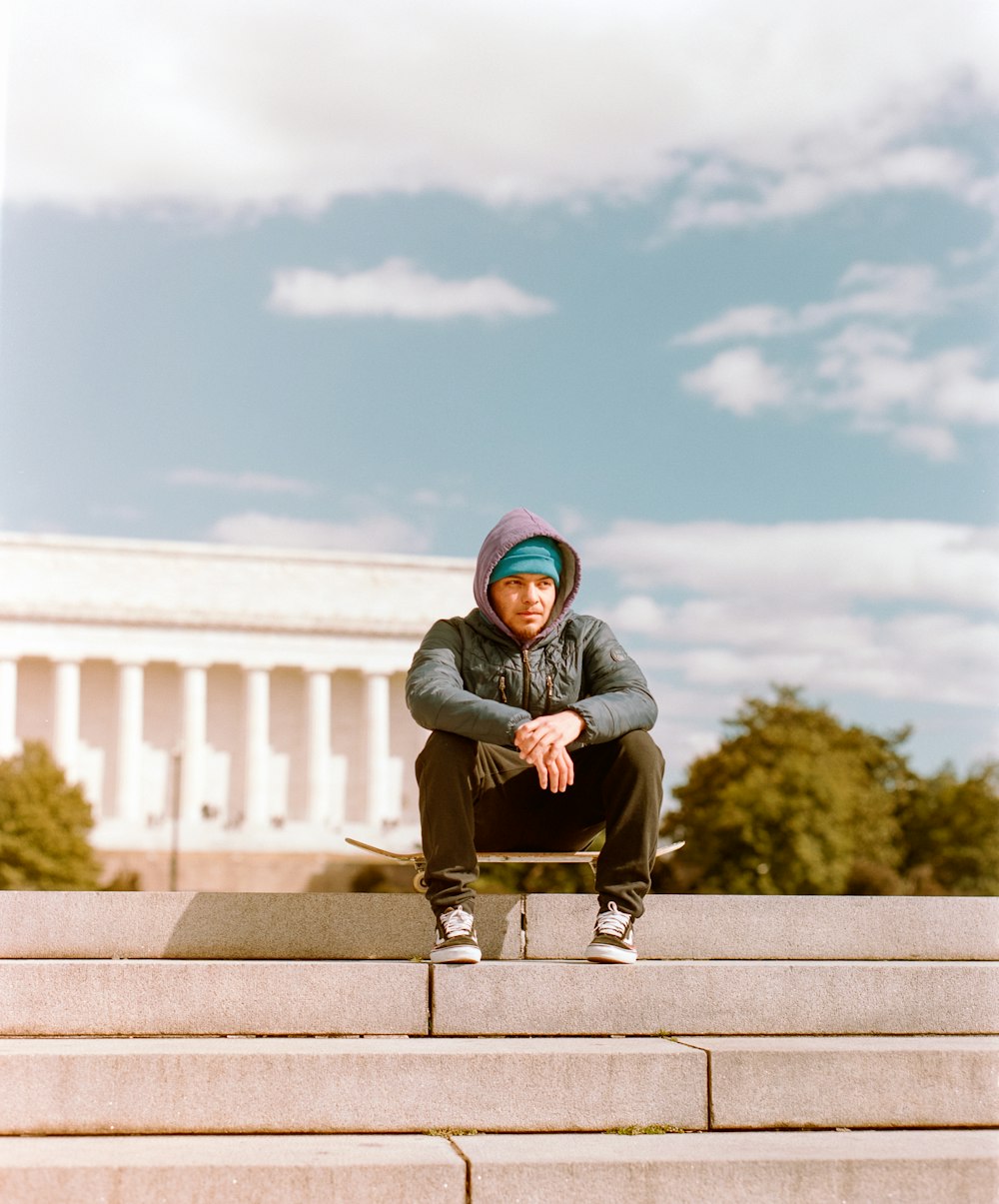 man in black hoodie sitting on concrete bench during daytime