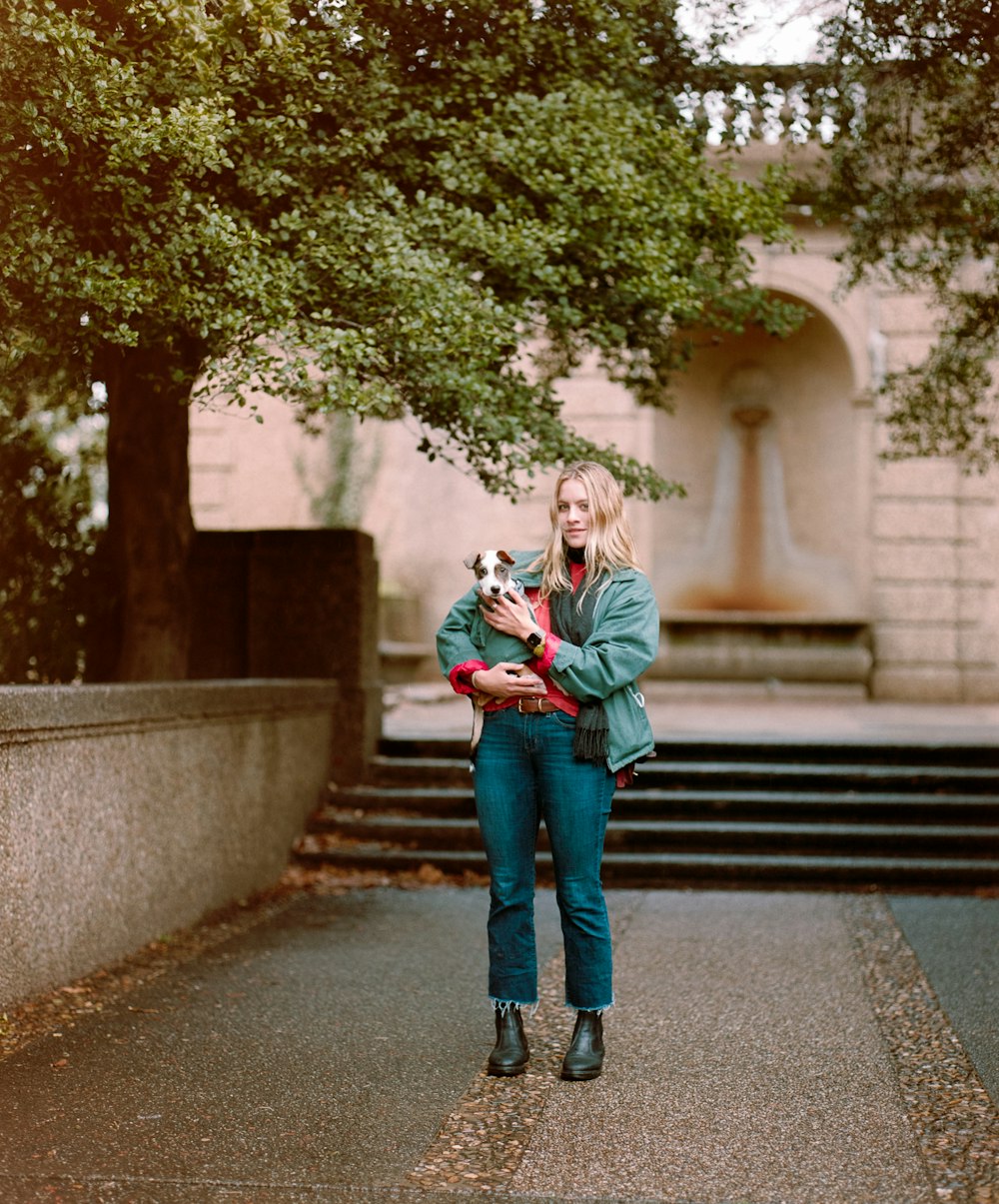 woman in green jacket and blue denim jeans standing on gray concrete stairs